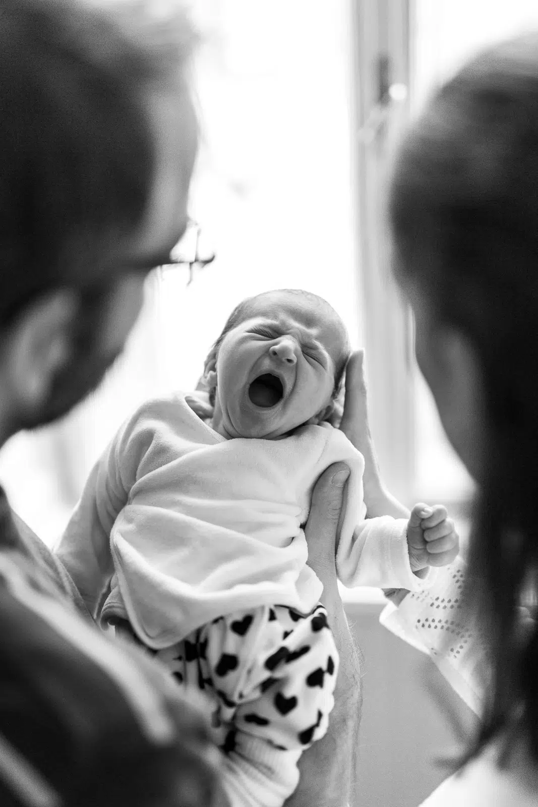 Foto eines gähnenden Babys, das von seinen Eltern gehalten wird