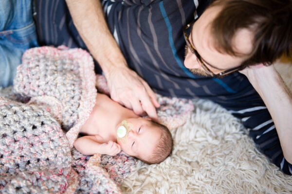 Vater und Baby mit Schnuller auf einem Teppich liegend