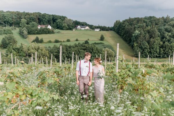 Ein sich ansehendes Brautpaar steht in einer sommerlichen Wiese mit Weinreben