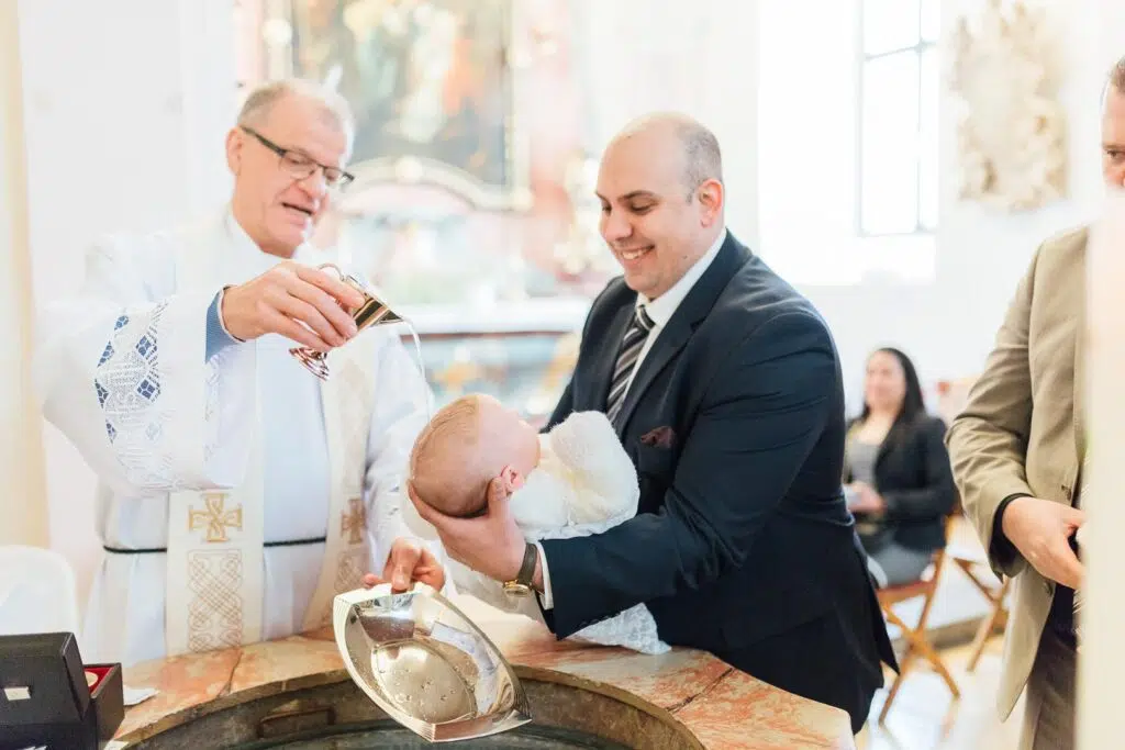 Taufzeremonie an einem Taufbecken mit Baby, Pfarrer und Taufpaten