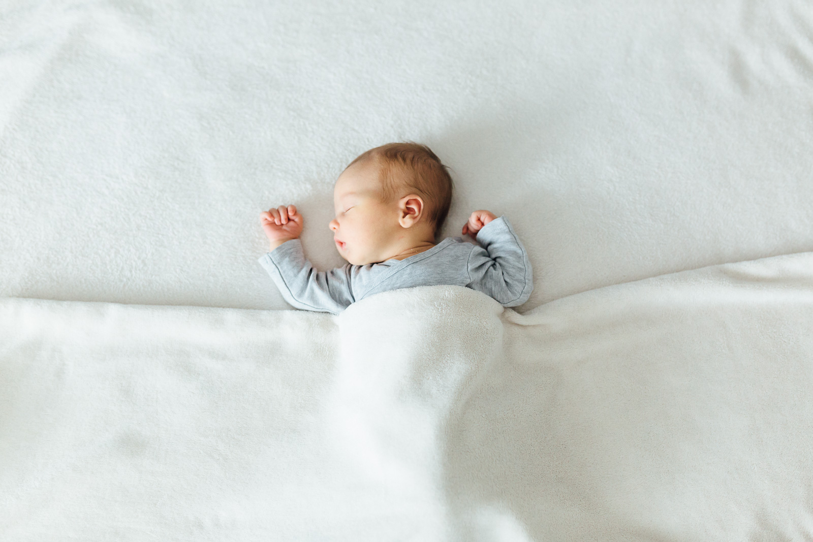 Neugeborenenfoto von einem Baby unter einer weißen Decke