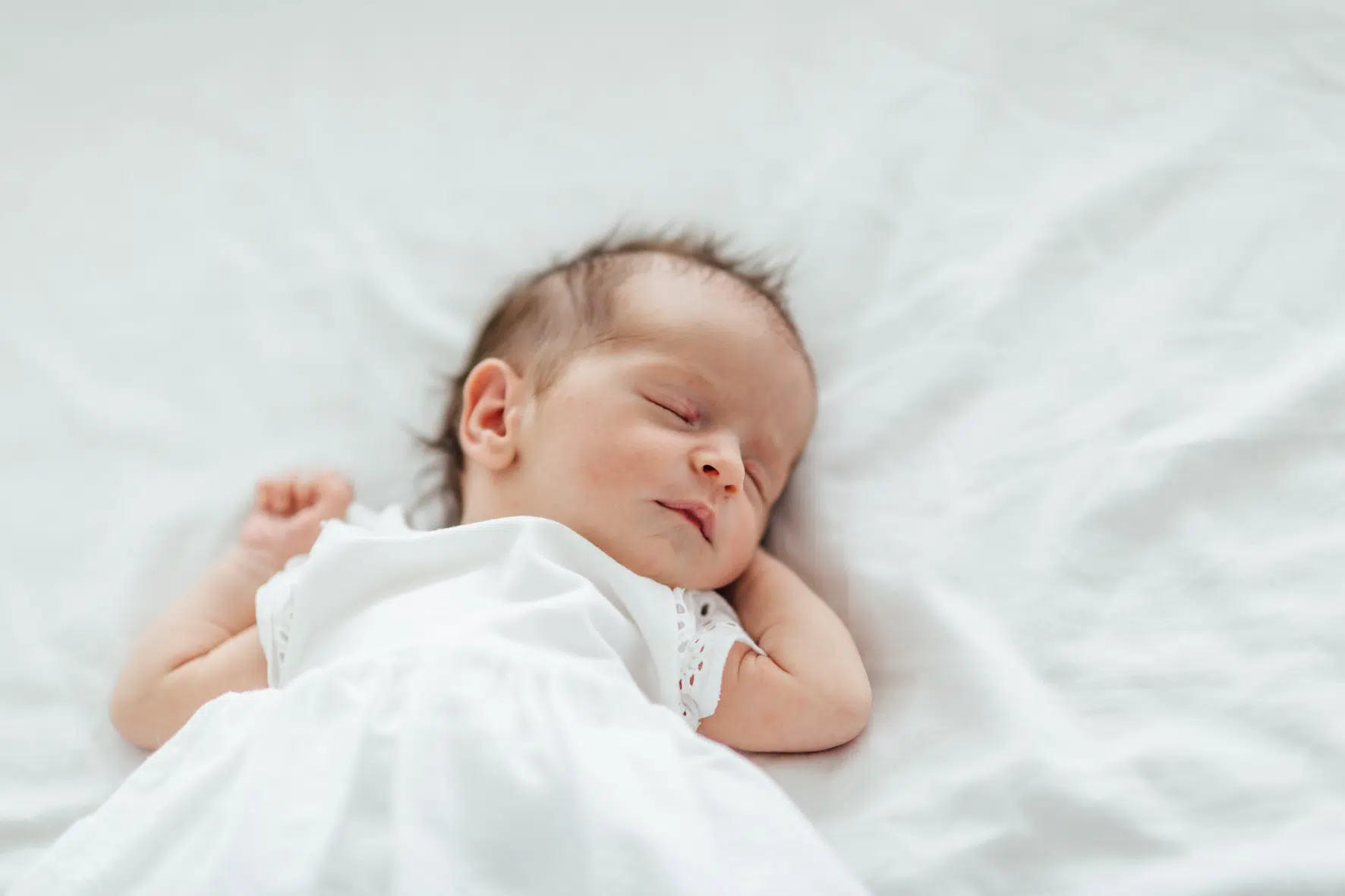 Newbornfotos von einem schlafenden, neugeborenen Babys in weißem Kleid