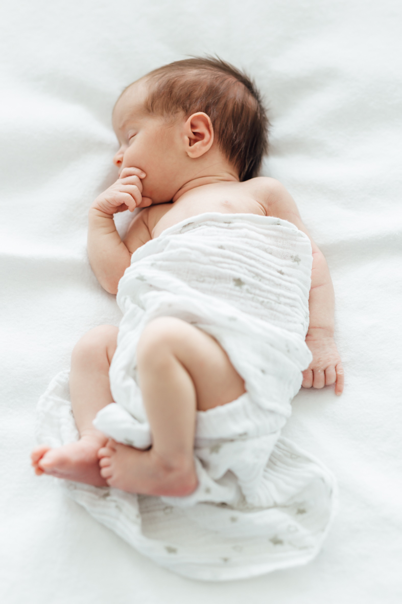 Ein in ein weißes Tuch gehülltes schlafendes Baby liegt auf einem weißen Untergrund