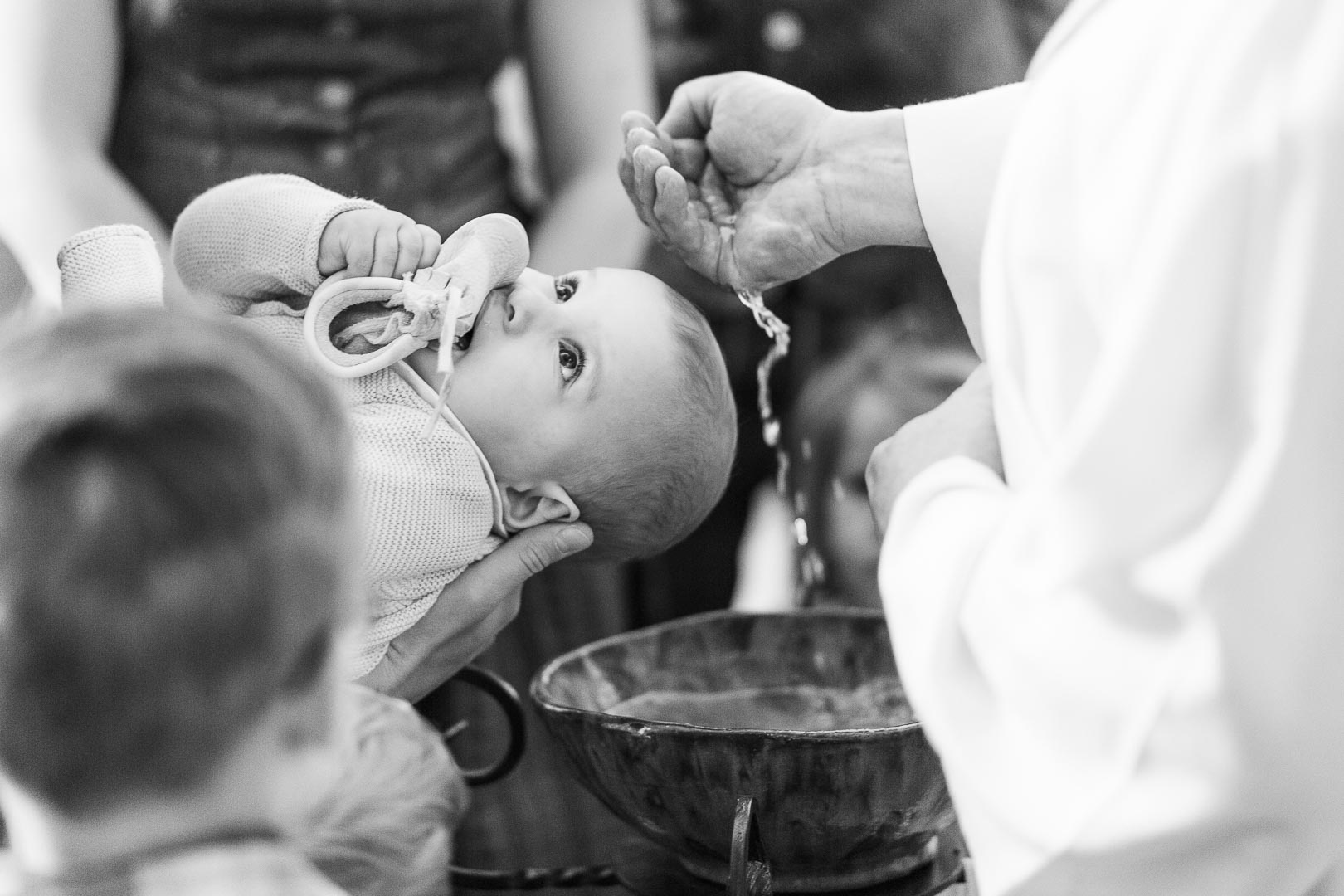 eine männliche Hand schöpft Wasser über den Kopf eines zu taufenden Babys
