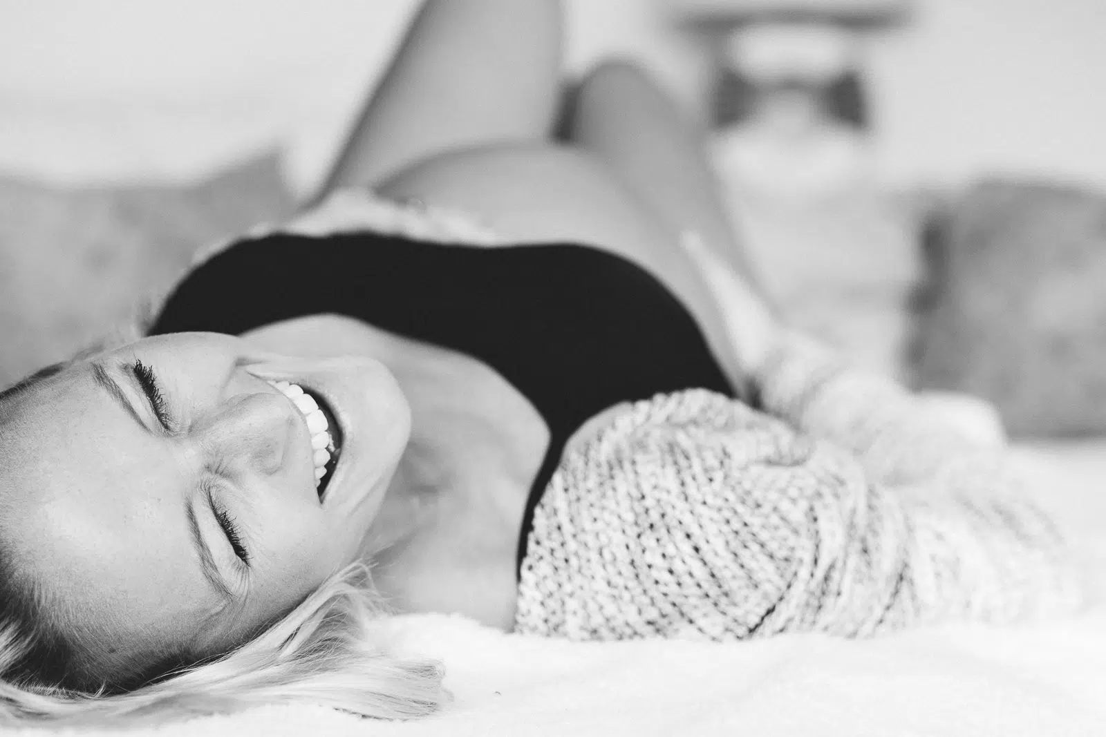 Lachende schwangere Frau, die auf dem Rücken liegt und ihren Bauch hält.