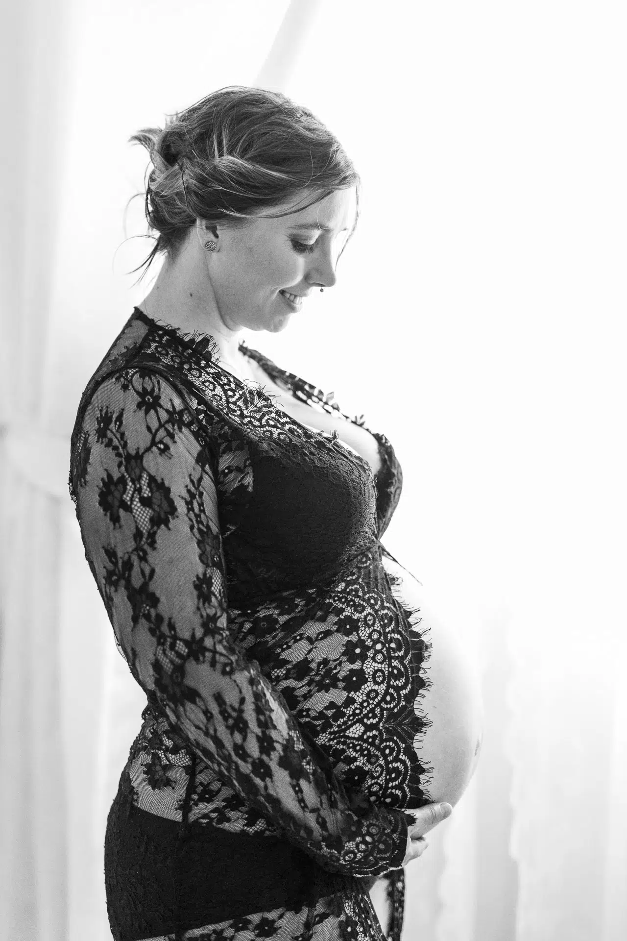 Profil einer schwangeren Frau in Spitzenkleid ihren Bauch haltend.