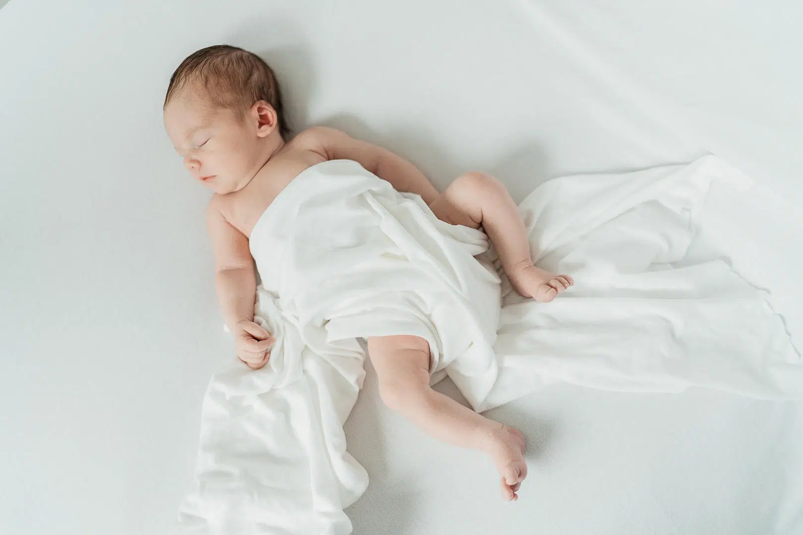 Newbornfoto von einem Baby mit weißem Tuch zugedeckt
