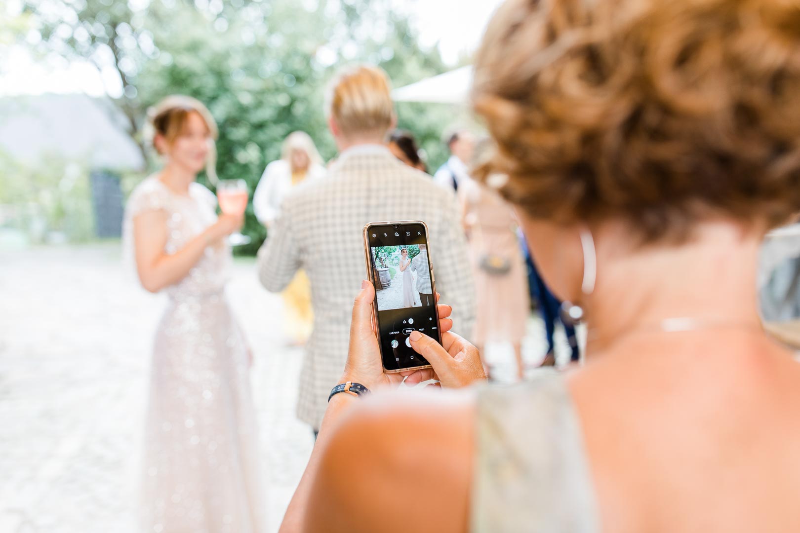Rückenansicht einer Frau, die mit dem Handy eine Braut fotografiert
