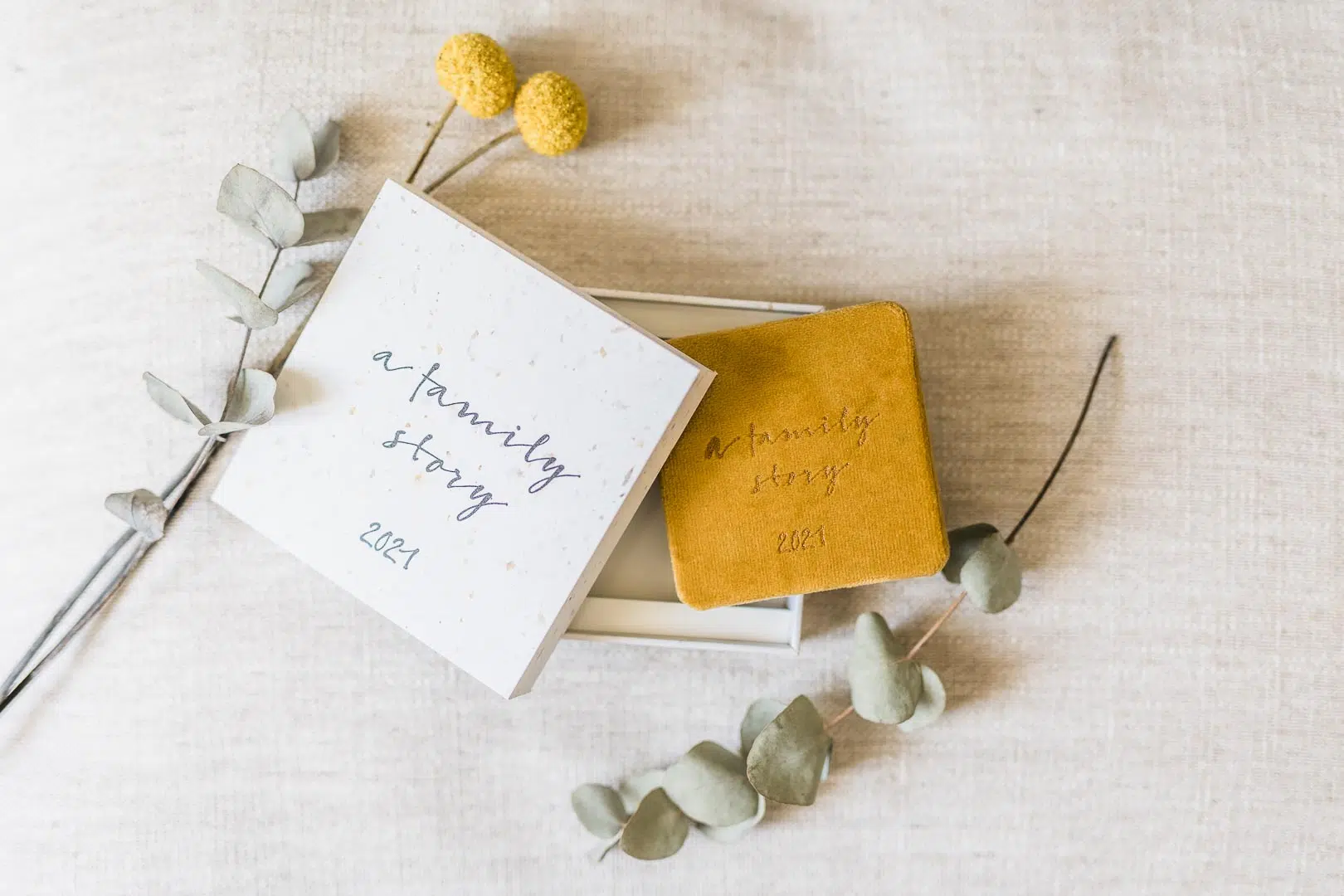 Minileporello in gelb mit einer Schachtel und Eukalyptus und gelben Blumen auf beigem Leinen