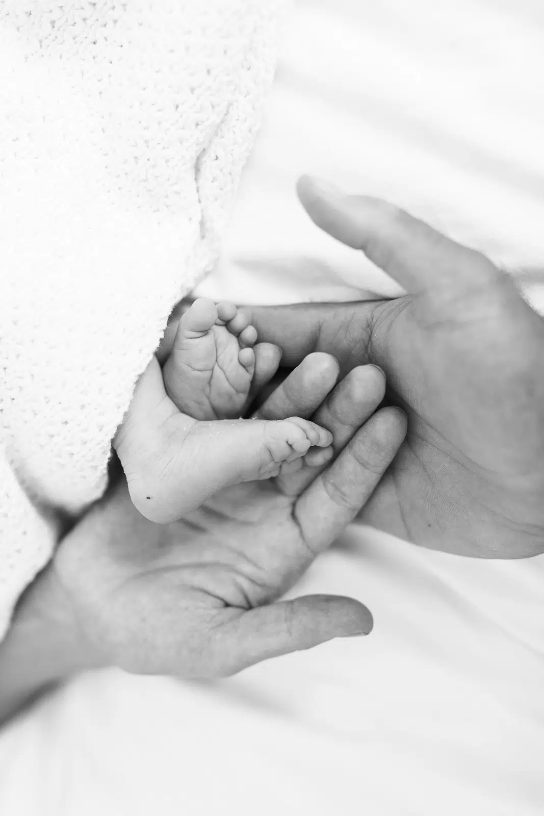 Gutschein-fuer-frischgebackene-Eltern Erwachsenenhände halten einen Babyfuß