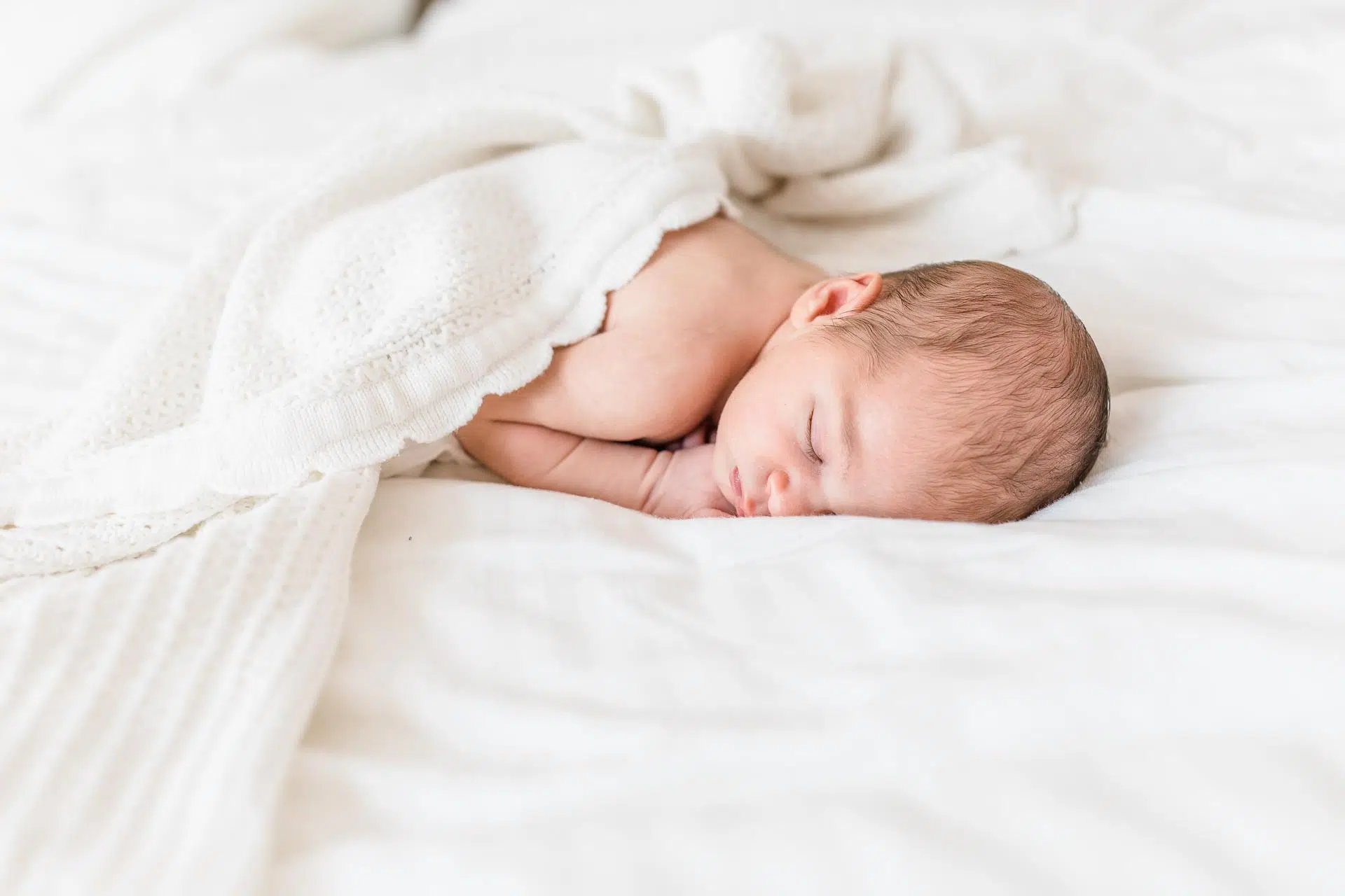 Geschenkidee-babyfotos - Carmen-Trappenberg-Fotografie-1 Ein neugeborenes Baby liegt unter einer weißen Decke