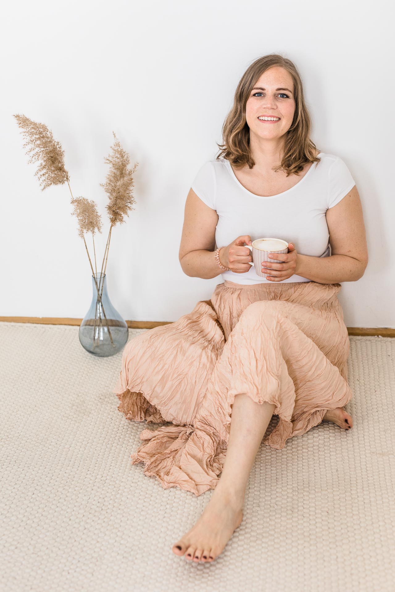 Businessportrait einer am Boden sitzenden Frau mit Tasse in den Händen