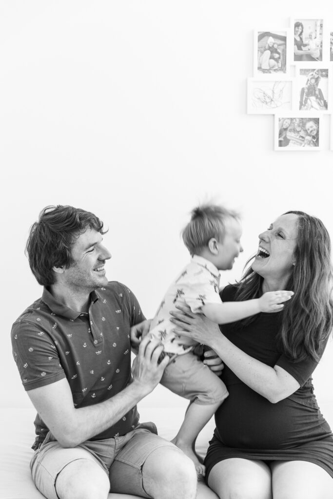 Lachende Familie mit Eltern und springendem Kleinkind.