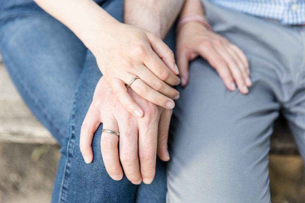 Nahaufnahme verschlungener Hände mit Ringen auf Beinen in Jeans abgelegt, Paarfotos im Prater.