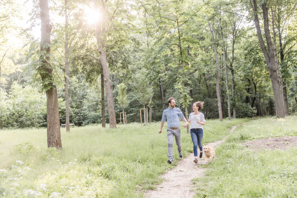 Weitwinkelaufnahme eines auf einem Waldweg laufenden Paares mit Hund.