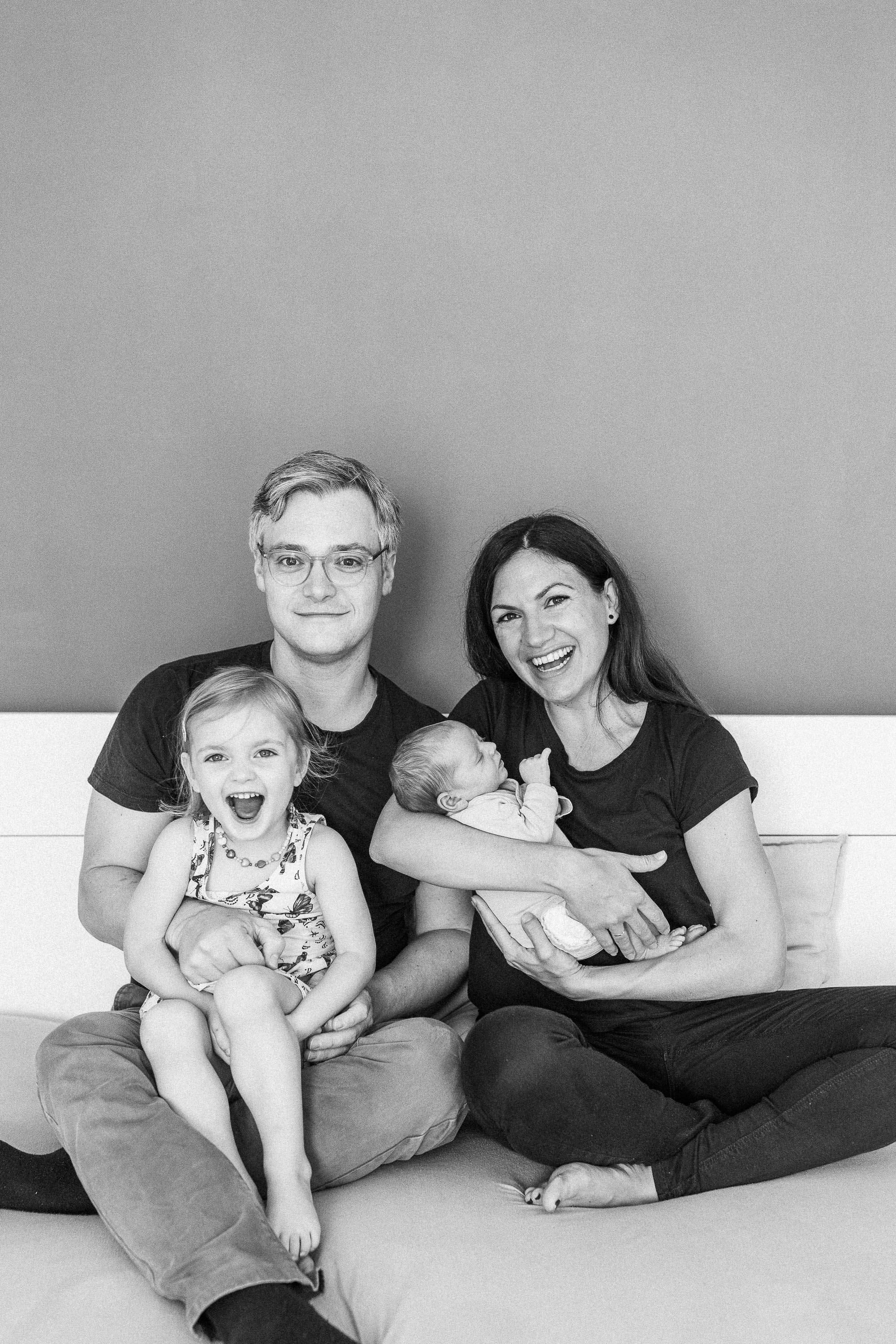 Lachende Familie mit Eltern, Kleinkind und Baby auf einem Bett.