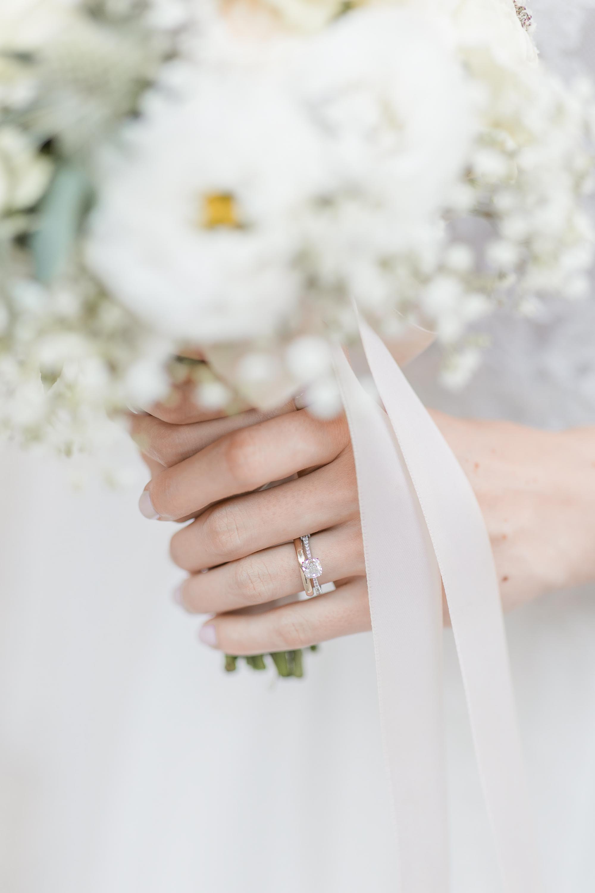Detailaufnahme einer weiblichen Hand mit Verlobungsring, Ehering und Brautstrauß.