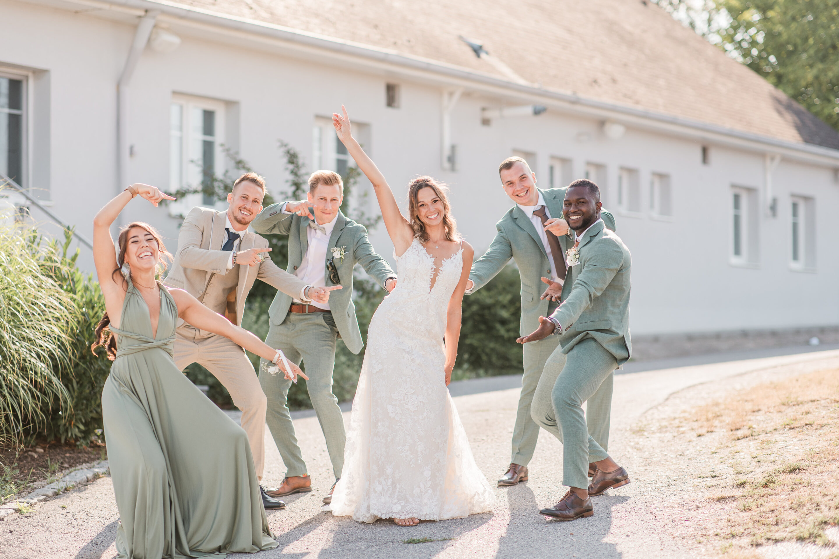 Brautpaar und Freunde bei einem Gruppenfoto auf einem Weg vor einem hellen Gebäude.